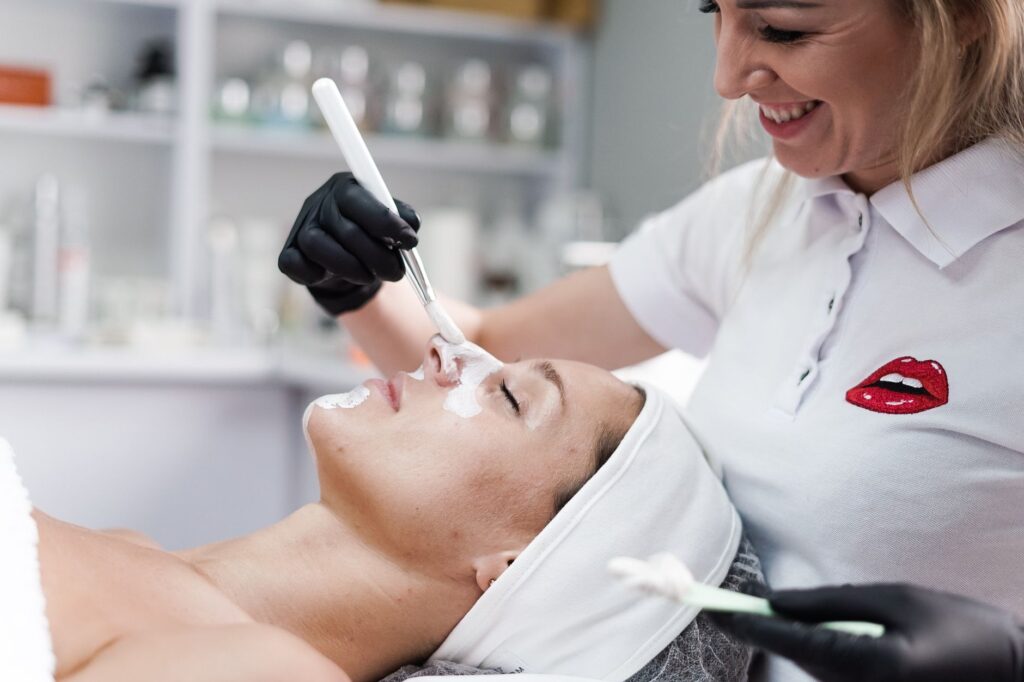 A beautician applying a face mask to a client in a salon, highlighting skincare and relaxation.