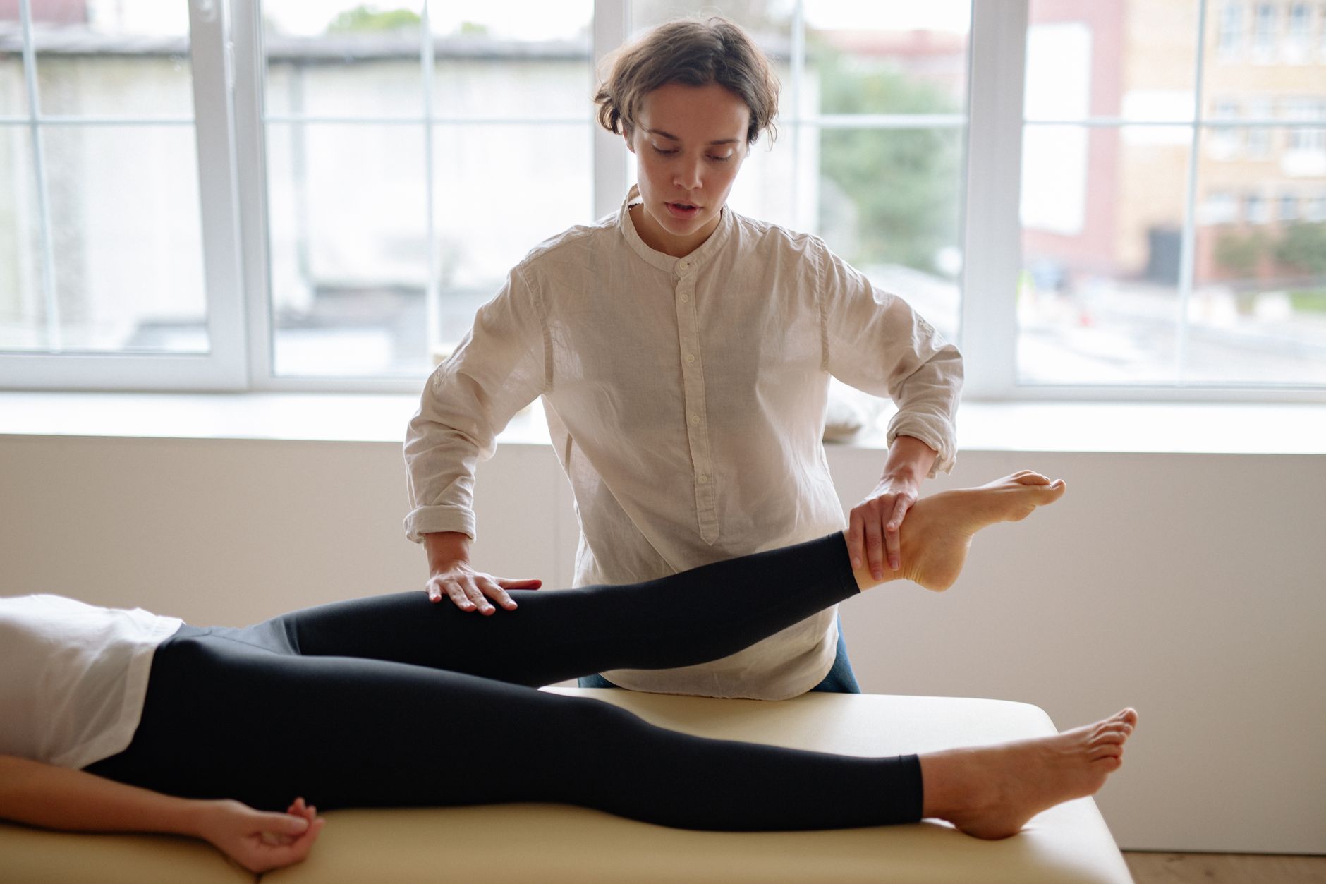 A therapist provides leg massage therapy to a client in a serene clinic setting.