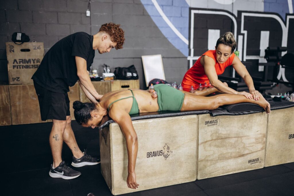 Athlete receives cupping therapy for muscle recovery in a gym setting with two therapists.